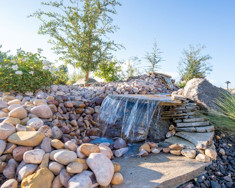 Flagstone spillway waterfall set in river rock with trees and white roses