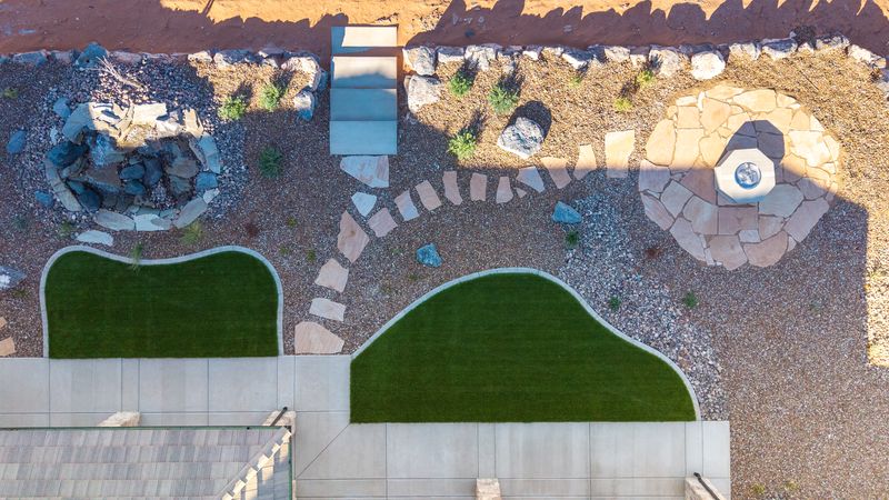 Overhead drone view of curved turf panels with concrete curbing, flagstone stepping stones, a flagstone fire pit patio, and a rock waterfall